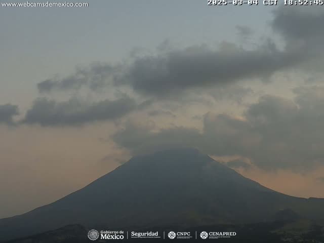 A large, dark mountain is visible beneath a mostly cloudy sky with a pale orange hue near the horizon.