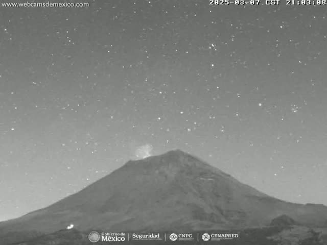 A large, dark mountain is seen under a night sky filled with stars, with a small eruption of light emanating from its peak.