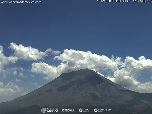 A partially snow-capped volcano is visible under a mostly clear blue sky with scattered cumulus clouds.