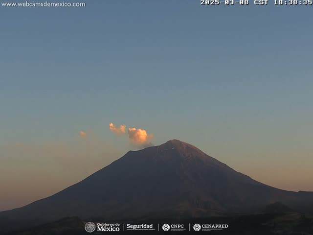 A large, dark volcano is visible against a twilight sky, with a small plume of smoke or ash emanating from its peak.