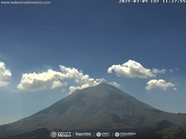 A large, dark-grey volcano is visible under a mostly clear sky with a few fluffy white clouds.