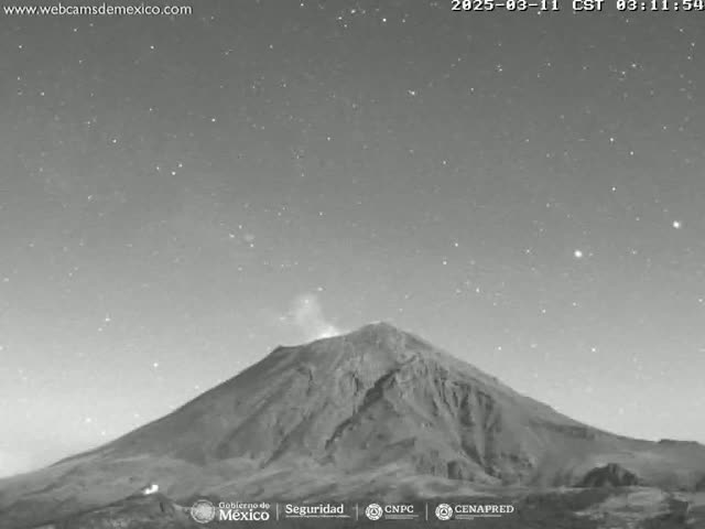 A grayscale nighttime image shows a large, dark mountain with a faint plume of smoke emanating from its peak under a clear, starry sky.