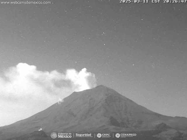 A nighttime, grayscale image shows a volcano emitting a plume of smoke under a clear, starry sky.