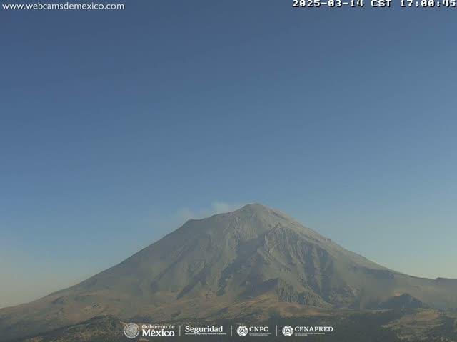 A large, gray volcano is visible under a clear, blue sky.