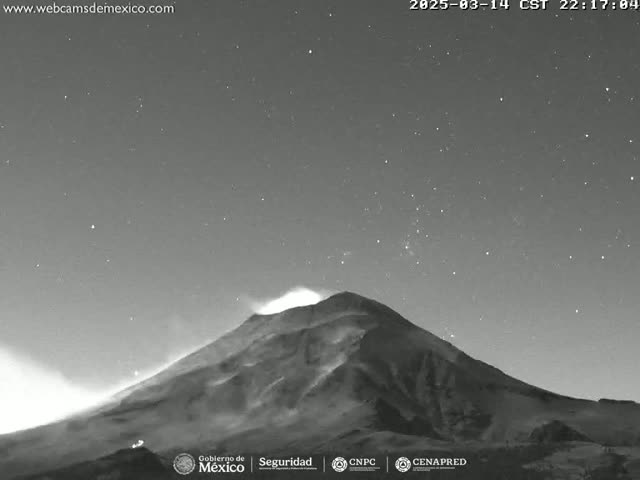 A nighttime, grayscale image shows a volcano erupting under a clear, starry sky.