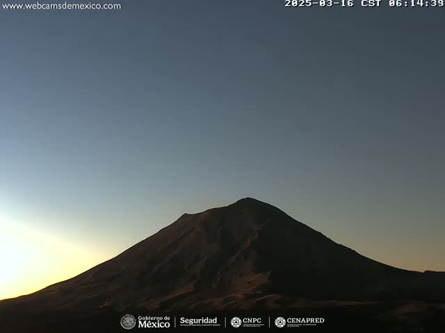 A dark, silhouetted volcano is seen at sunrise under a clear sky.