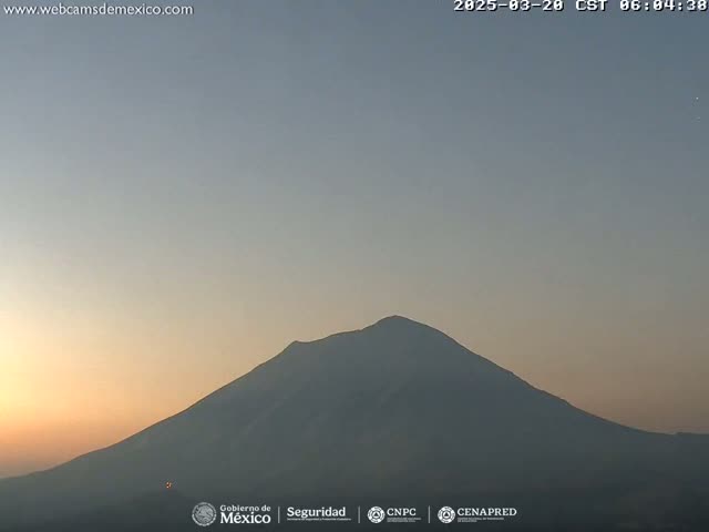 A large, dark-colored mountain is silhouetted against a pale orange and gray sunrise sky.