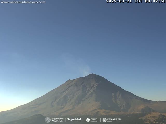 A large, dark-colored volcano with a small plume of smoke is visible under a clear blue sky.