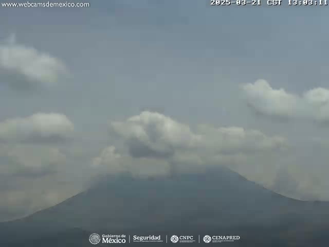 A mostly cloudy sky overlooks a large, hazy mountain.