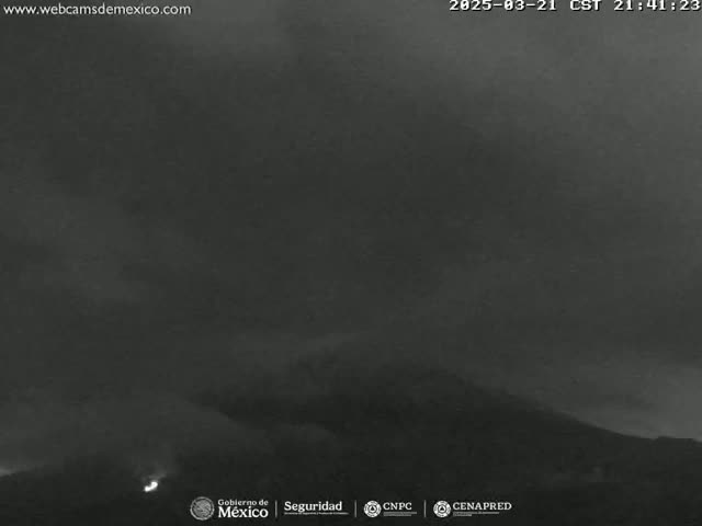 A nighttime long shot shows a volcano erupting under a dark, cloudy sky.