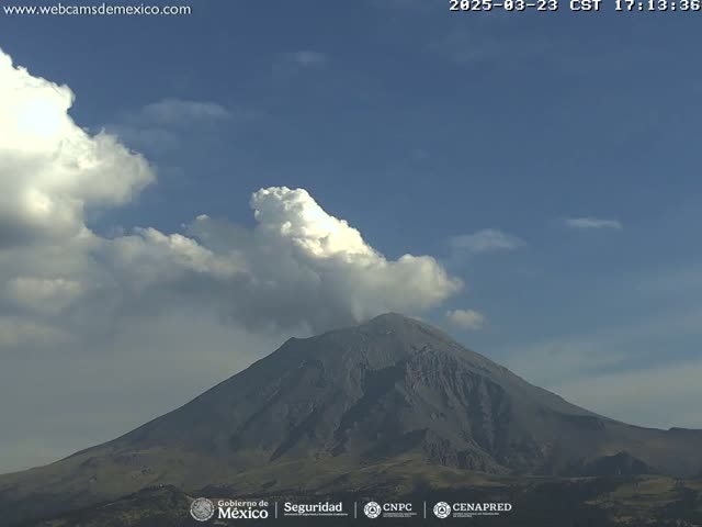 A large, dark-grey volcano is visible under a partly cloudy sky.