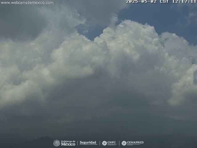 A mostly cloudy sky with dark, looming clouds in the distance over a low-lying landmass.
