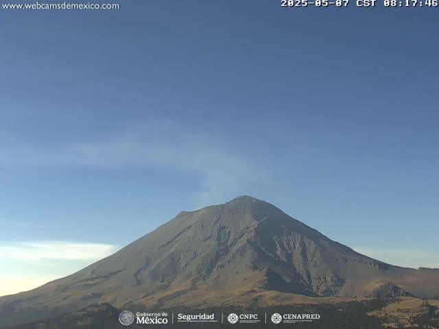 A large, gray volcanic mountain is visible under a clear, light-blue sky.