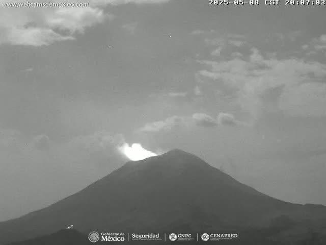 A grayscale image shows a volcano erupting a small plume of smoke under a partly cloudy sky.