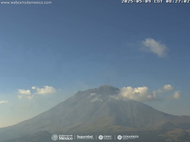 A partially cloudy sky overlooks a large, hazy mountain with a hint of snow near its peak.