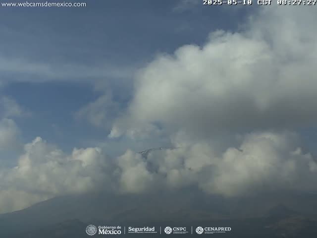 A snow-capped mountain is partially obscured by a mostly cloudy sky.