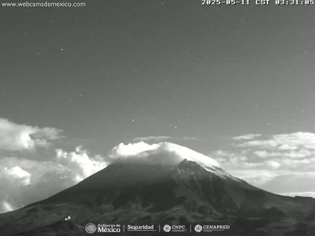 A snow-capped mountain is partially obscured by clouds under a partly cloudy night sky.