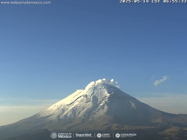A snow-capped volcano emits a plume of smoke under a clear blue sky.