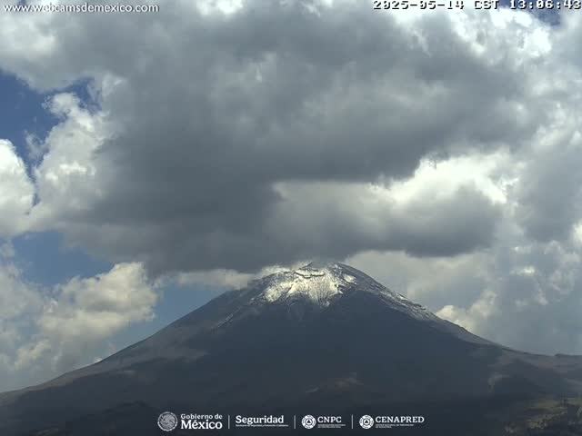 A snow-capped mountain is partially obscured by a mostly cloudy sky.
