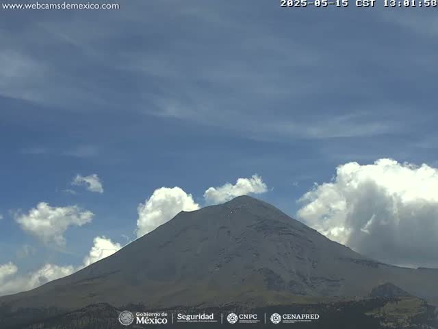 A large, grey mountain is visible under a mostly clear blue sky with some fluffy white clouds.