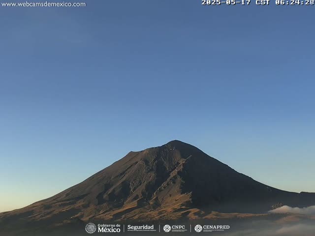 A dark-colored, large mountain is visible under a clear, blue sky with a low-lying layer of fog or clouds at its base.
