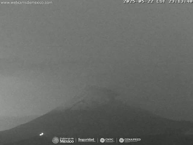 A nighttime, hazy view of a large, dark mountain under a gray sky.