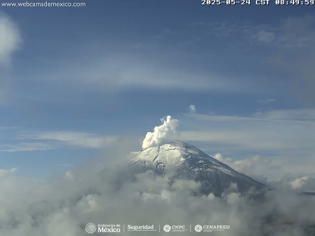 A snow-capped volcano erupts a plume of smoke under a mostly clear sky.