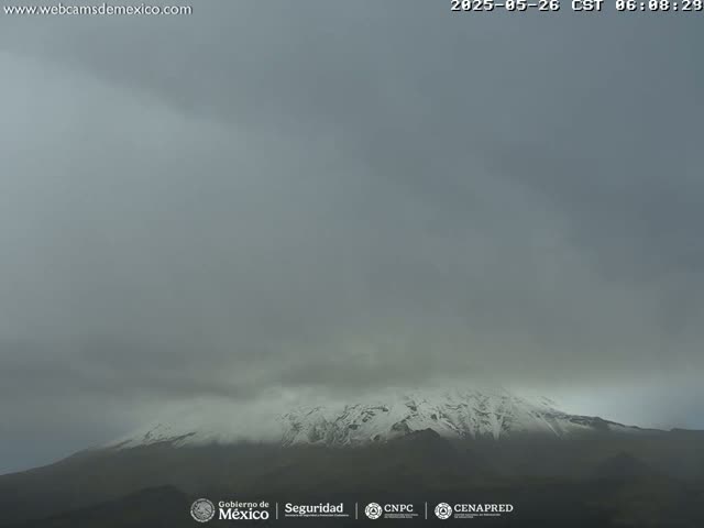 A snow-capped mountain is partially obscured by a hazy, overcast sky.