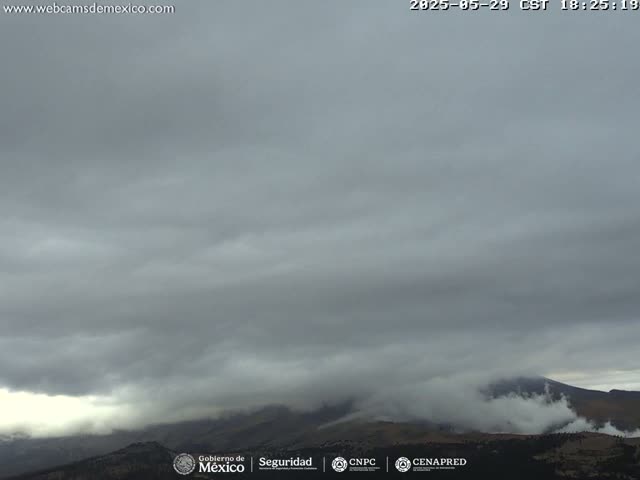 A cloudy sky obscures a mountain range partially covered in fog or low clouds.