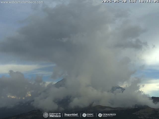 A partially cloudy sky obscures a mountain peak shrouded in fog or low clouds.