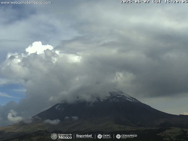 A snow-capped mountain is partially obscured by a cloudy, overcast sky.