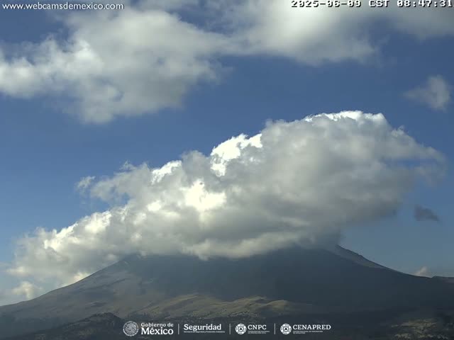 A large, fluffy cumulus cloud partially obscures a dark mountain under a mostly clear blue sky.