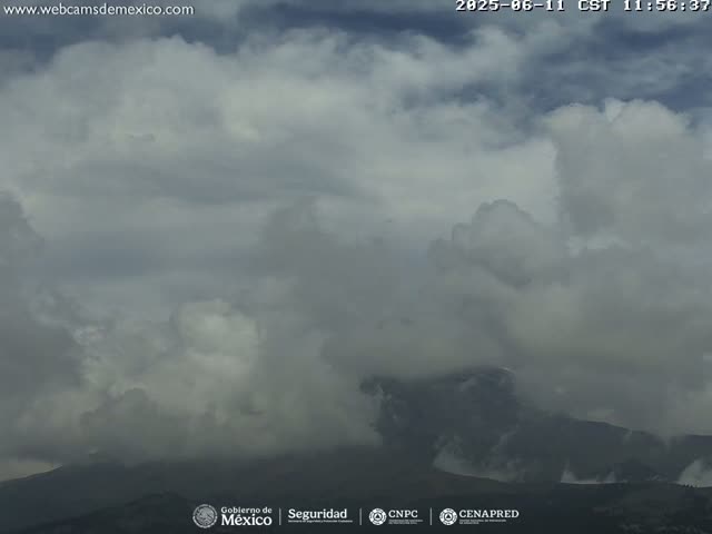 A mostly cloudy sky with dark, puffy clouds obscures a mountain range in the distance.