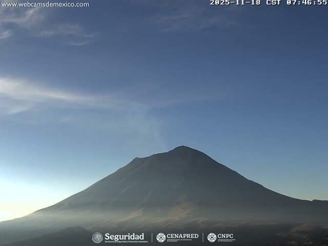 A grayscale night vision image displays a dark volcano actively emitting a bright plume of gas under a clear, starry night sky.