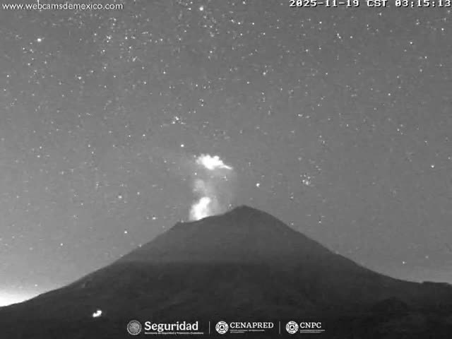 A dark volcano emits a bright plume of smoke and ash under a clear, star-filled night sky, with small glowing spots visible on its lower flank.