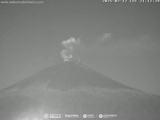 A nighttime grayscale image shows a volcano erupting under a mostly clear sky.