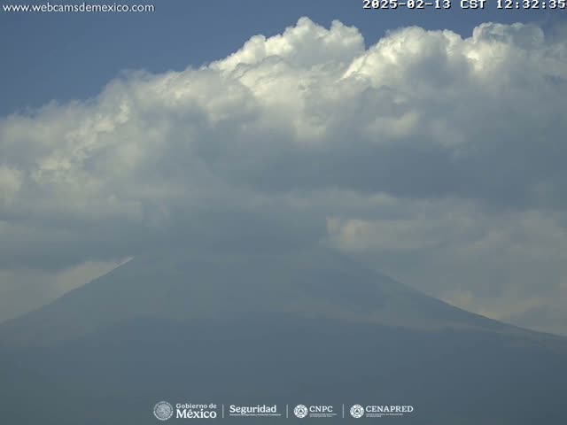 A large, partially cloudy sky hangs over a hazy, dark-grey mountain.