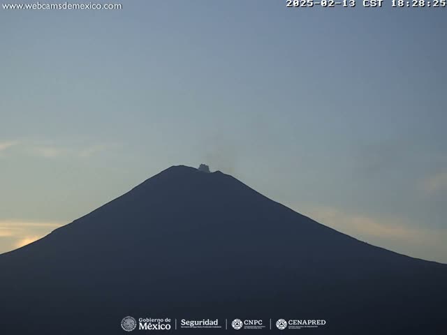 A dark, silhouetted volcano with a small plume of smoke erupting from its peak is visible against a pale twilight sky.
