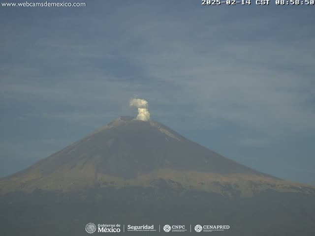 A large volcano with a small plume of smoke erupting from its peak under a mostly clear sky.
