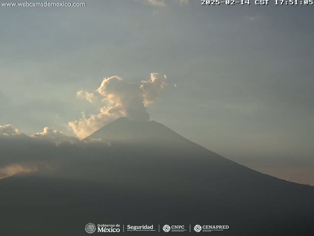 A large, dark mountain is partially obscured by light gray clouds under a mostly clear sky.