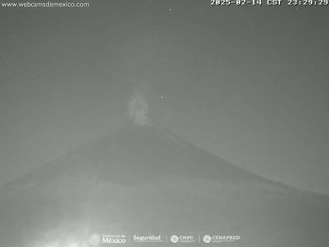 A nighttime, low-light image shows a volcano emitting a plume of smoke under a clear, starry sky.