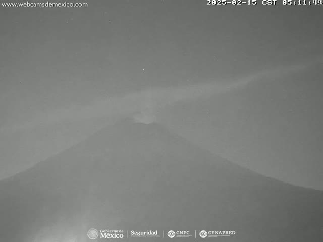 A nighttime, low-light image shows a volcano erupting a plume of ash and smoke into the night sky.