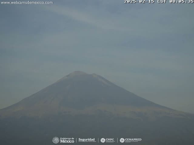 A hazy, distant view of a snow-capped mountain is seen on a slightly cloudy day.