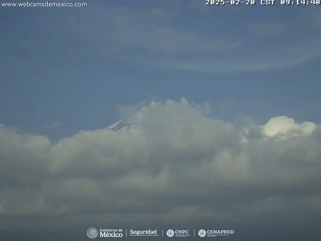 A snow-capped mountain peak is partially obscured by a mostly cloudy sky.