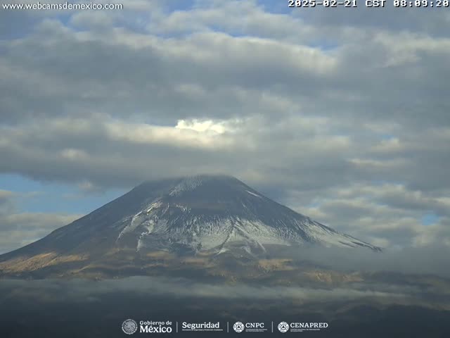 A snow-capped volcano is partially obscured by a partly cloudy sky.