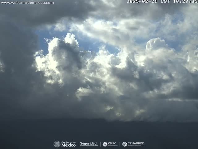 A mostly cloudy sky with some breaks of sunlight reveals a dark, distant landscape.
