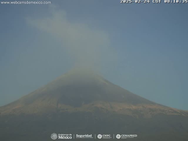 A volcano is seen emitting a plume of smoke under a clear, hazy sky.