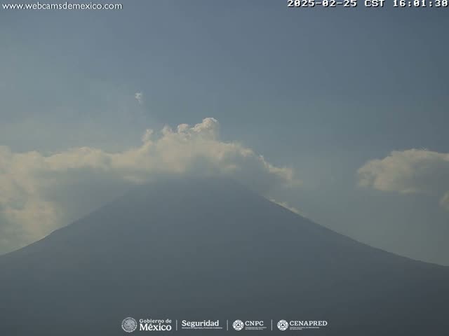 A large, dark mountain is partially obscured by a layer of light gray clouds under a mostly clear sky.