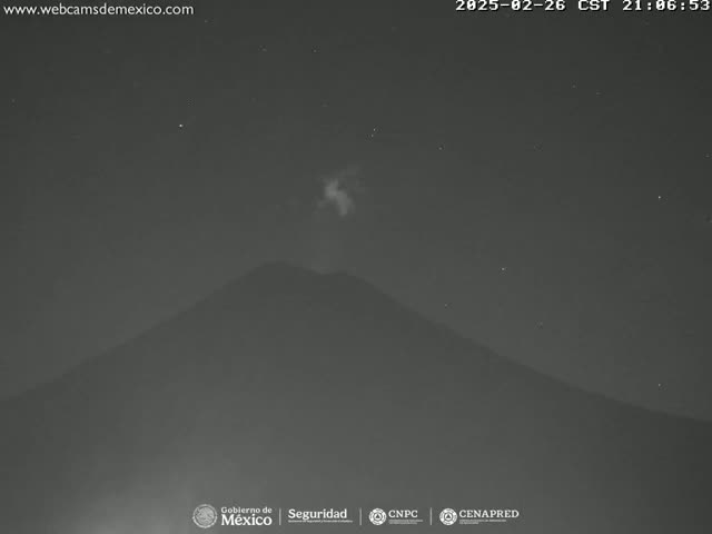A nighttime, low-light image shows a volcano with a faint plume of smoke or ash rising from its summit under a clear, starry sky.