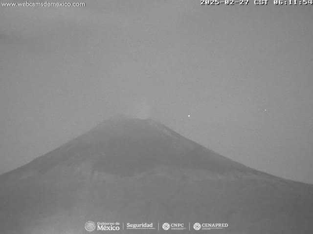 A grayscale image shows a volcano emitting a faint plume under a hazy, overcast sky.
